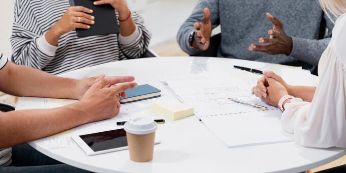 a group of people sitting around a table with papers and pens