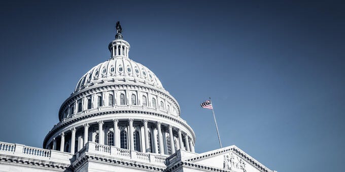 a white building with a flag on top with United States Capitol in the background