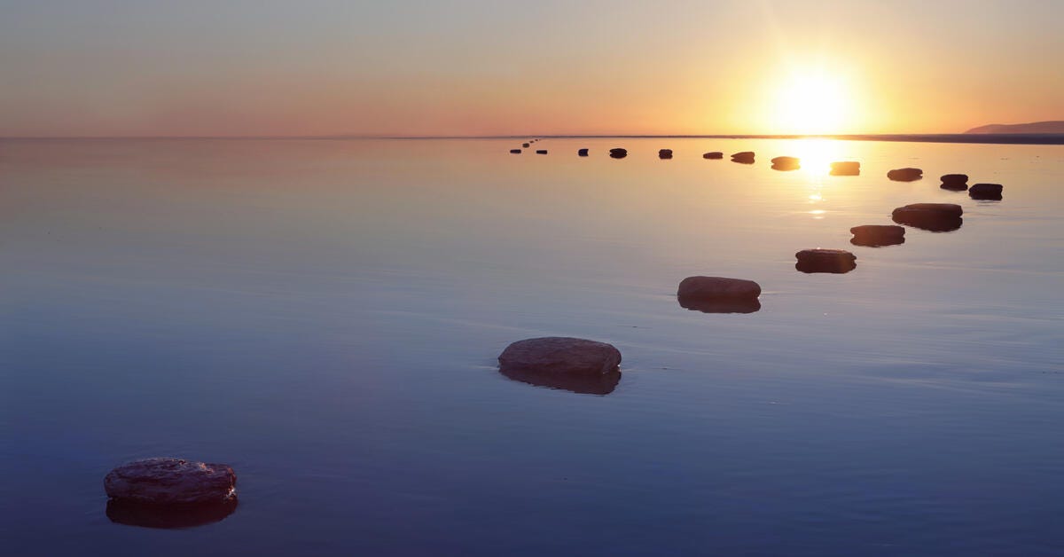 a body of water with rocks in it and the sun setting